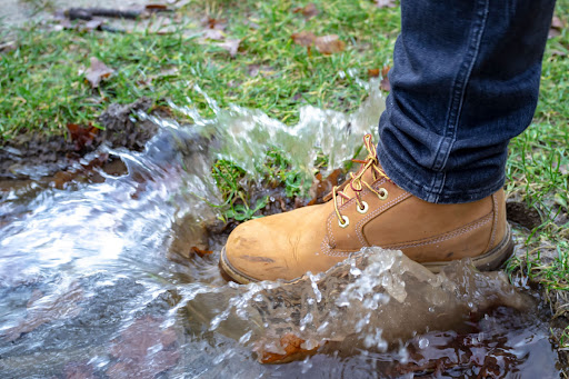 A booted foot stepping into a large muddy puddle.