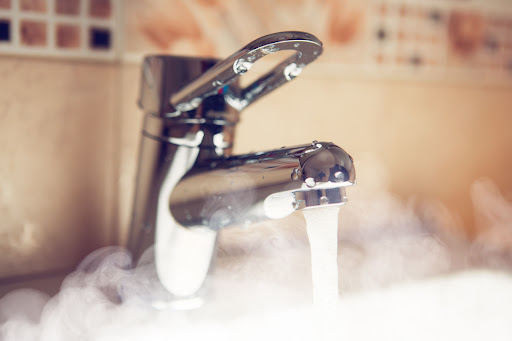A faucet running hot water with steam.