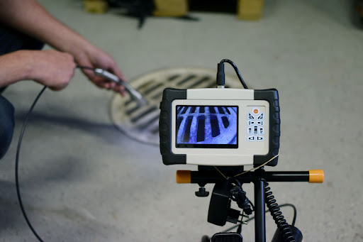 A person inserting a sewer inspection camera into a drain. There is a camera feed showing a live video from the camera.