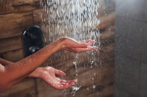 A person feeling the water fall from a rainfall shower head.