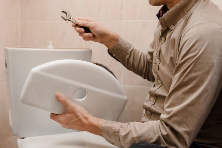 Homeowner holding toilet tank cover in one hand and wrench in the other hand while attempting to fix his running toilet.
